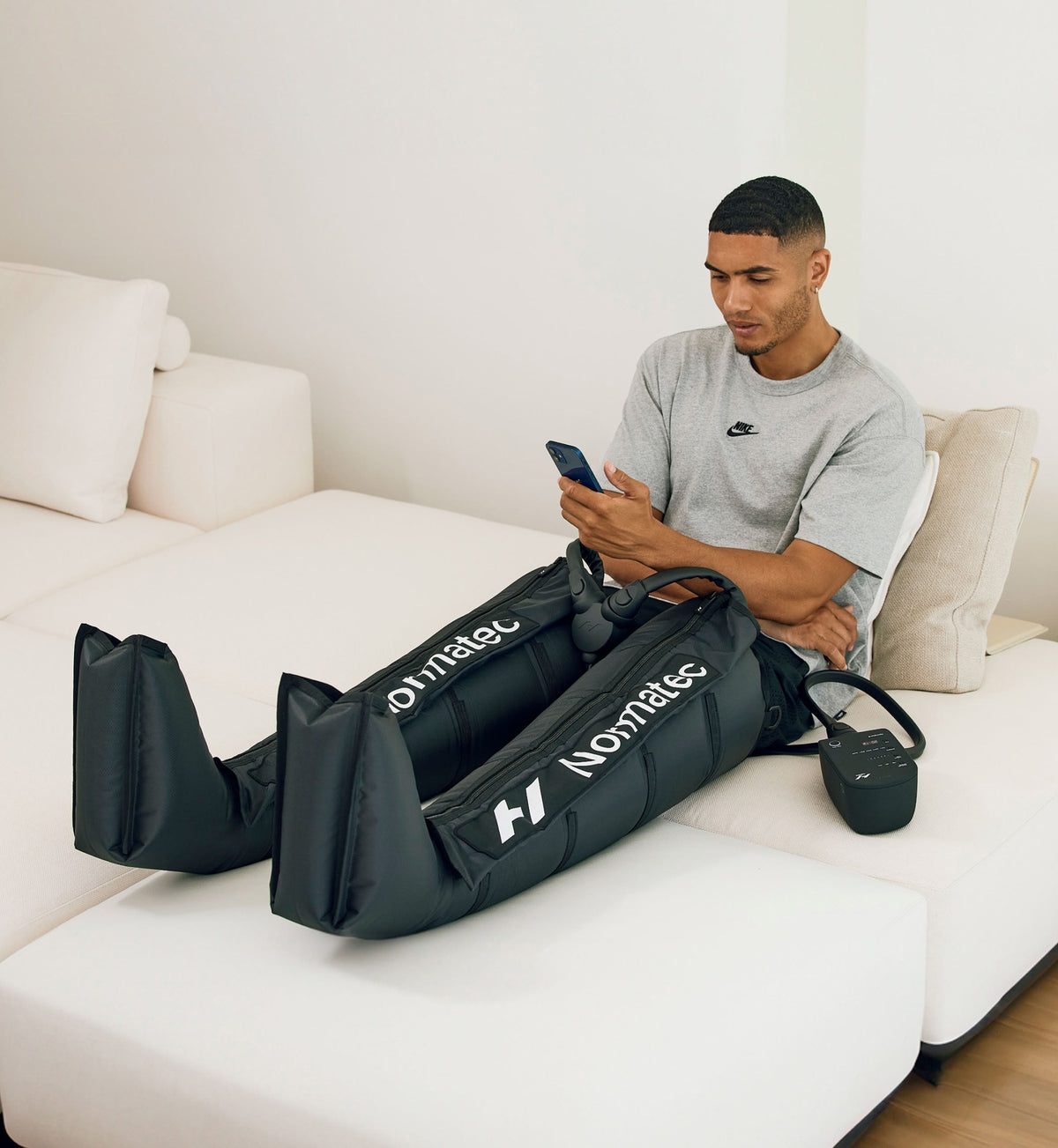 Man sitter i en soffa med mobilen och har Normatec 3 Legs på benen